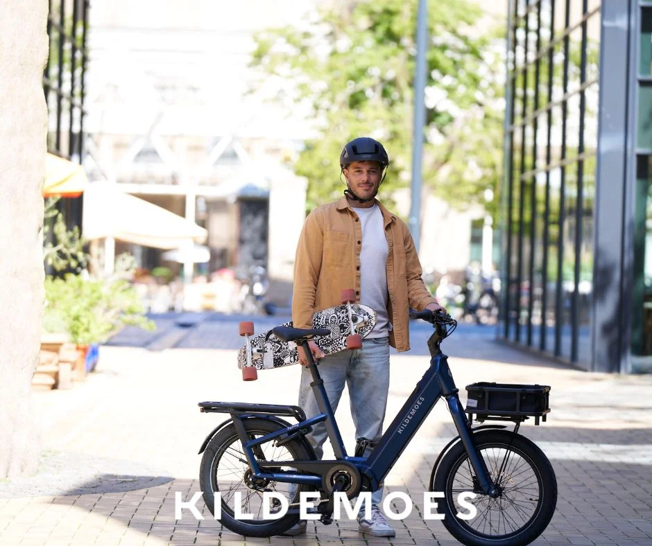 Mand med cykelhjelm står med en Kildemoes elcykel med bagagebærer i byen